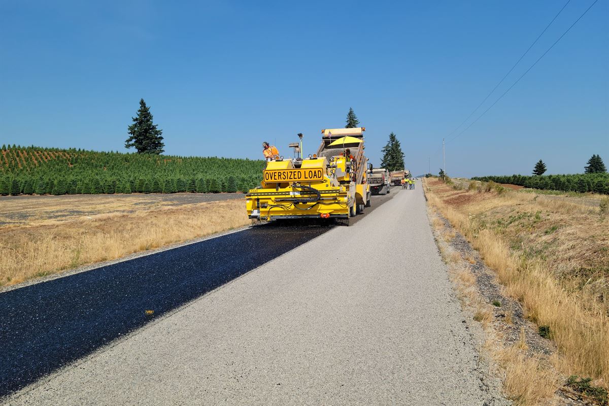 Asphalt paver laying fresh pavement on a long rural road