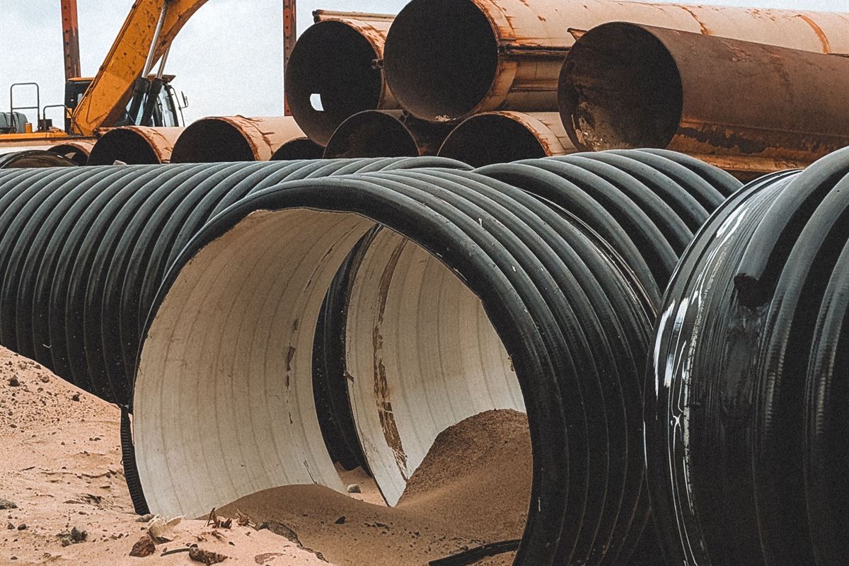 Large corrugated storm pipe staged on a graded site beside an excavator
