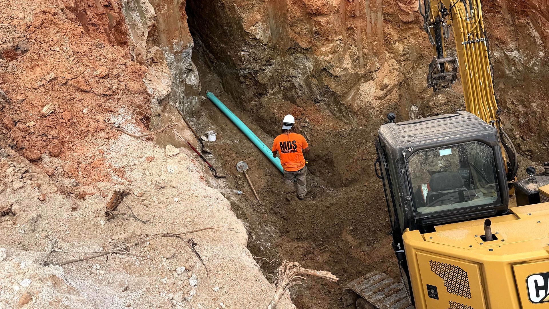 Crew member laying green PVC pipe in a deep trench beside a compact excavator in Alpharetta, Georgia