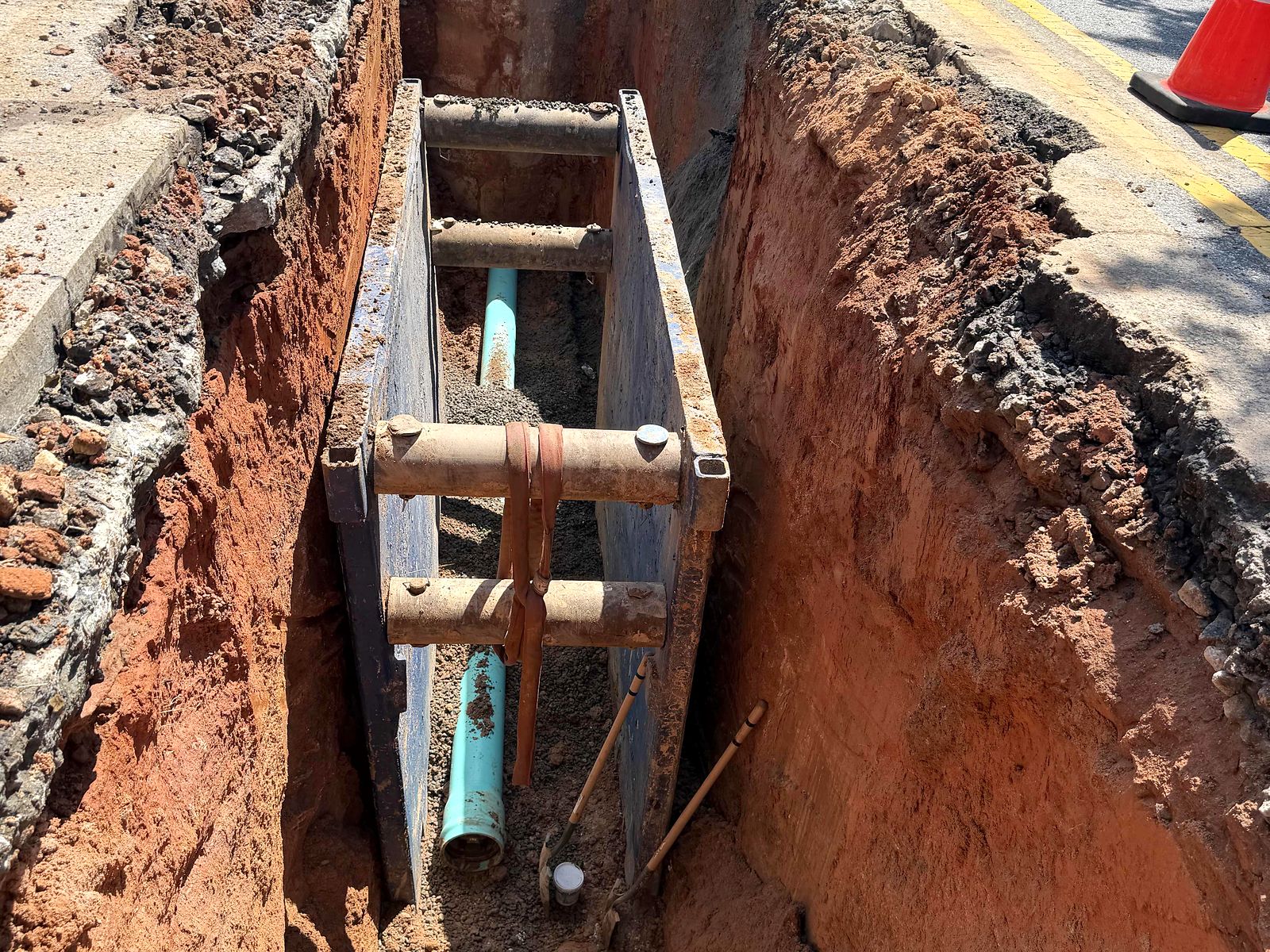 Trench box and green PVC pipe in a trench cut along a public street in Alpharetta, Georgia