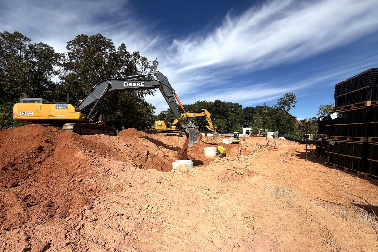 Excavator digging beside precast manholes and stacked underground stormwater modules on a commercial site in Alpharetta, Georgia