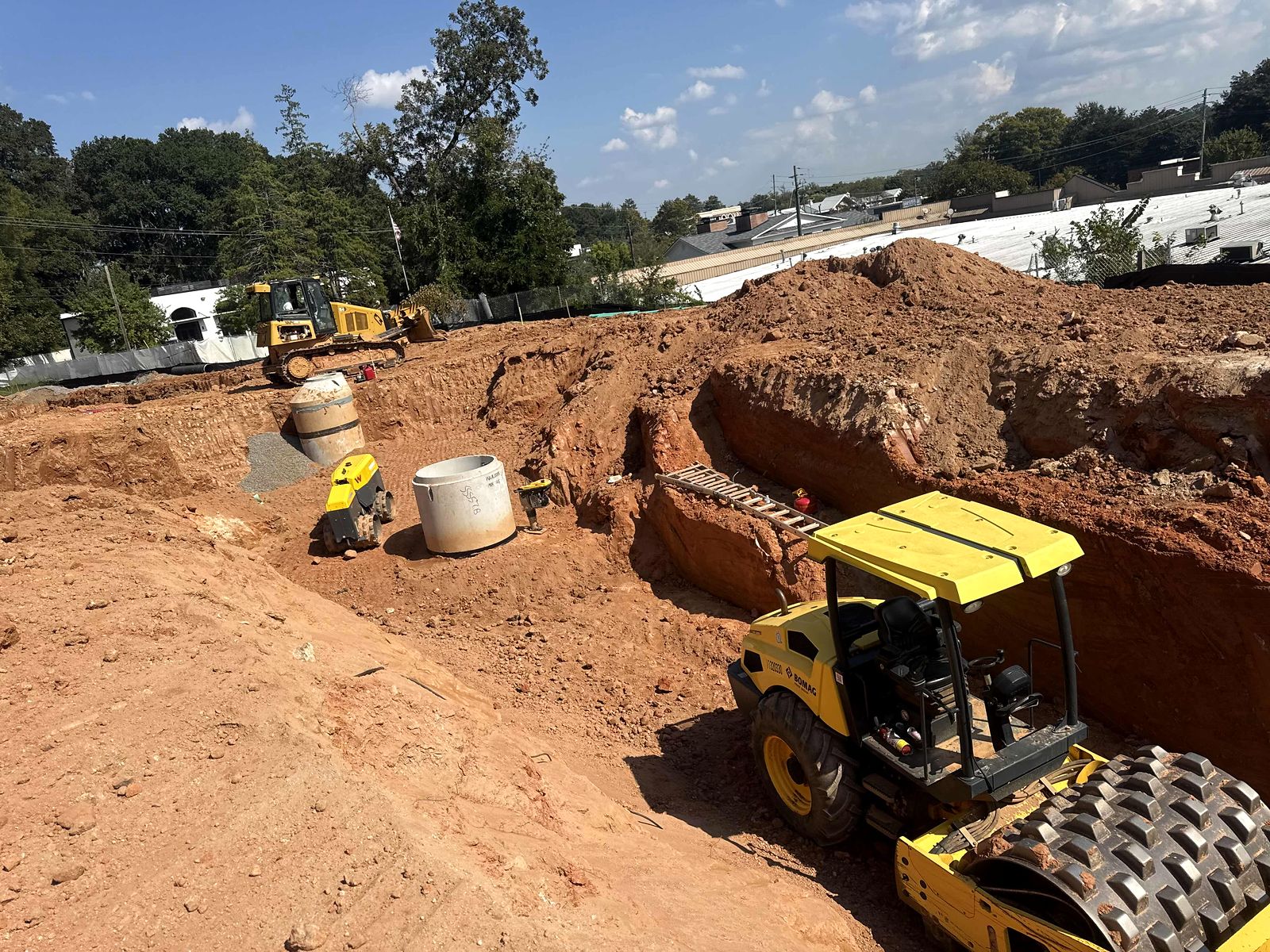 Roller compacting soil near precast manhole sections and an open excavation in Alpharetta, Georgia