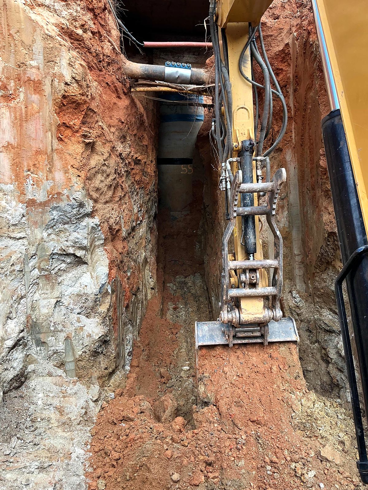 Excavator bucket in a narrow trench below existing utility lines in Alpharetta, Georgia