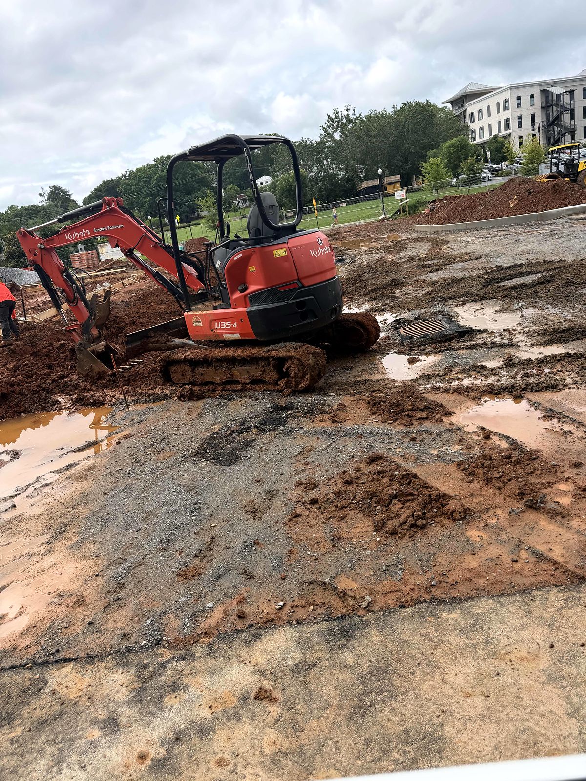 Compact excavator on a wet site beside a storm drain inlet at Reliant Market District