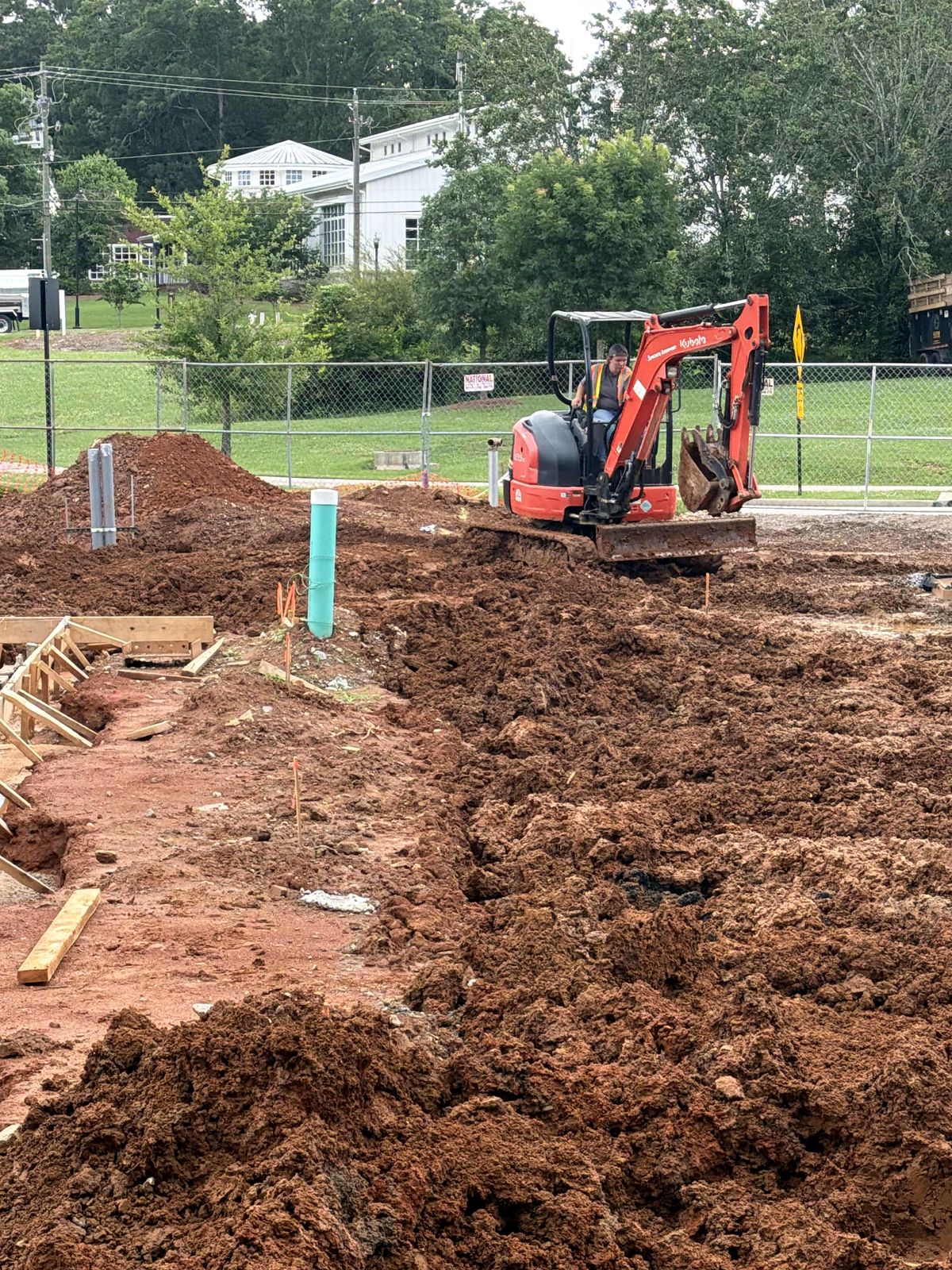 Compact excavator grading a building pad with a PVC cleanout and wood formwork at Reliant Market District