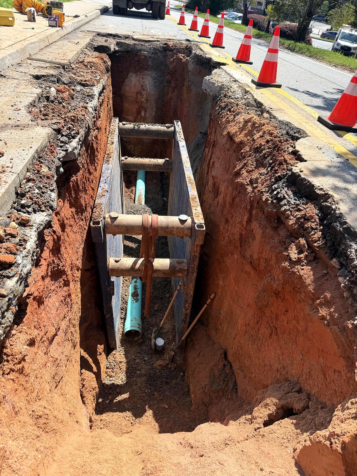 Trench box and green PVC pipe in a trench cut along a public street in Alpharetta, Georgia