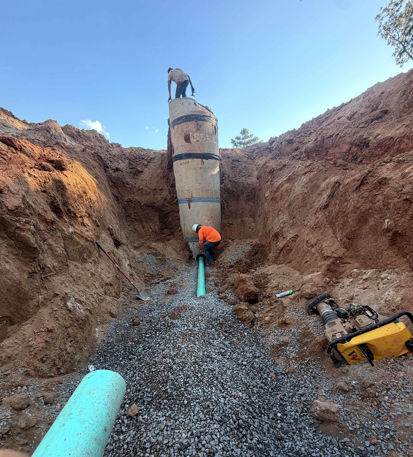 Crew setting a precast manhole on gravel bedding with green PVC pipe in Alpharetta, Georgia