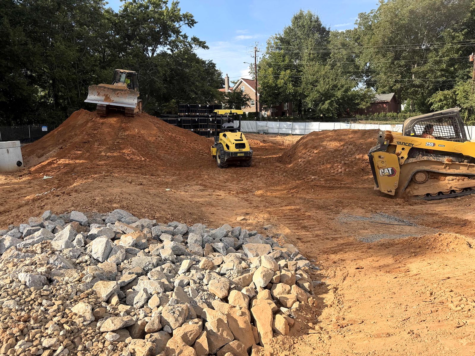 Dozer, roller, and skid steer grading a commercial site in Alpharetta, Georgia, beside a pile of rip rap