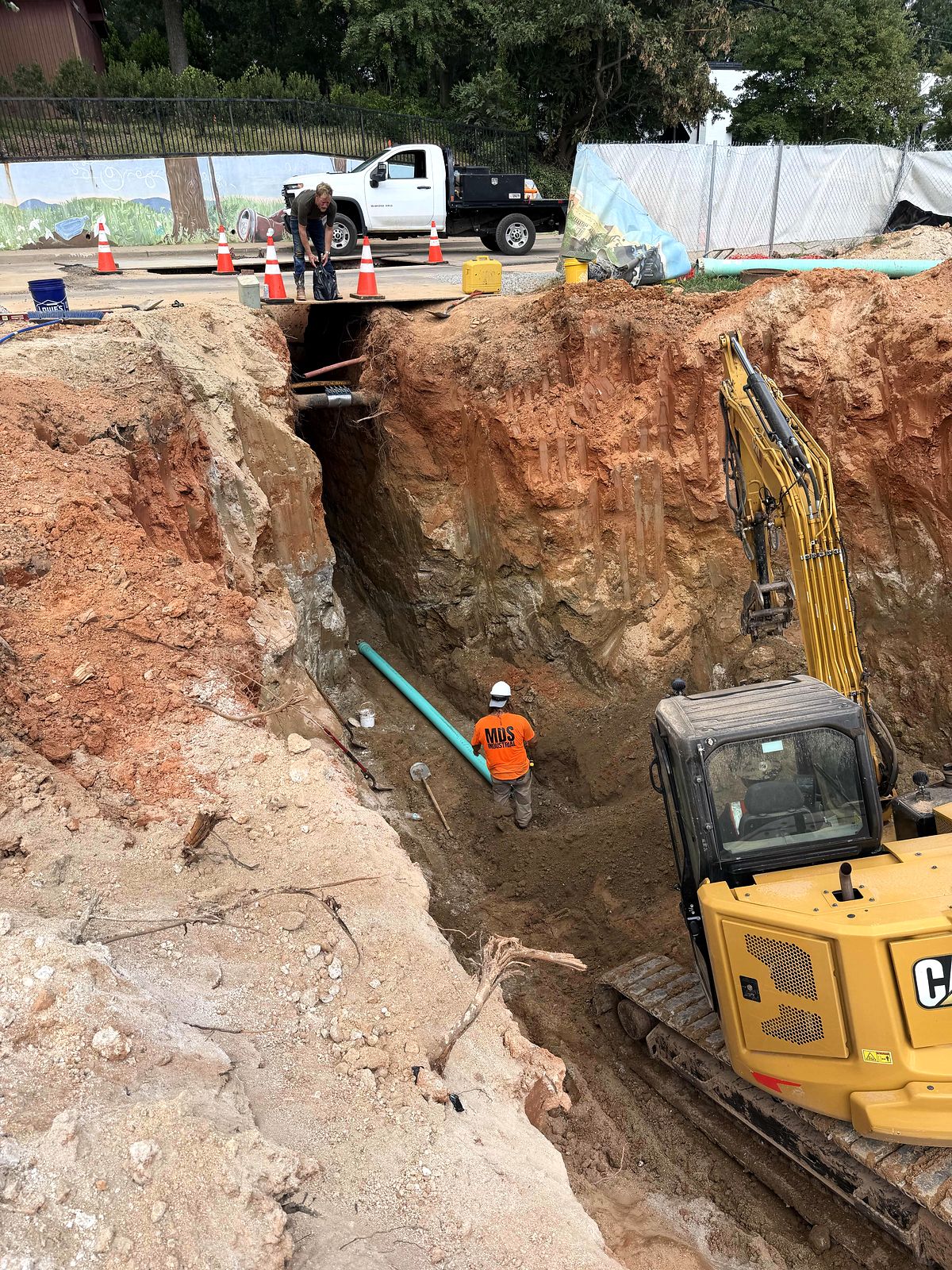 Crew member laying green PVC pipe in a deep trench beside a compact excavator in Alpharetta, Georgia