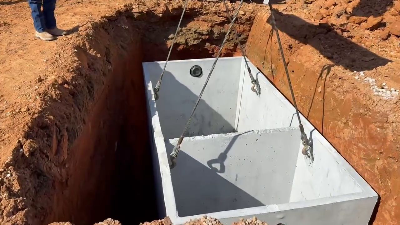 A boom truck lowers a two-compartment precast concrete tank into a trench at the Twigs Farmers Market site.